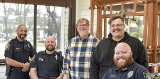 Awaiting their cuts are (L-R in uniform) Officer Eddie Hernandez, Officer Eric Tilley and Officer Tyler Simpson. Barber Sam Burch is standing left in the yellow checkered shirt beside barber Tyler Powell. Photo/Fayetteville PD.