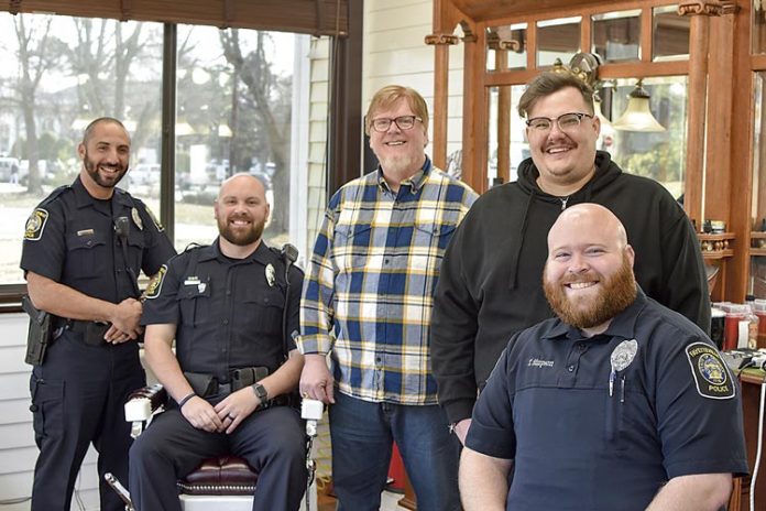 Awaiting their cuts are (L-R in uniform) Officer Eddie Hernandez, Officer Eric Tilley and Officer Tyler Simpson. Barber Sam Burch is standing left in the yellow checkered shirt beside barber Tyler Powell. Photo/Fayetteville PD.