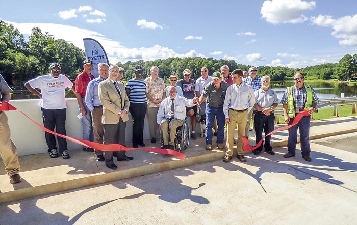 County staff and officials (including county commission Chairman Eric Maxwell cutting the ribbon and Commissioner Chuck Oddo nearby at left), project representatives and a group of neighbors attended the Aug. 30 ribbon cutting for the $3 million Emerald Lake Dam project funded by 2017 SPLOST (special purpose local options sales tax) dollars. The new dam and spillway southeast of Fayetteville was designed to meet Category 1 dam standards. Photo/Ben Nelms.