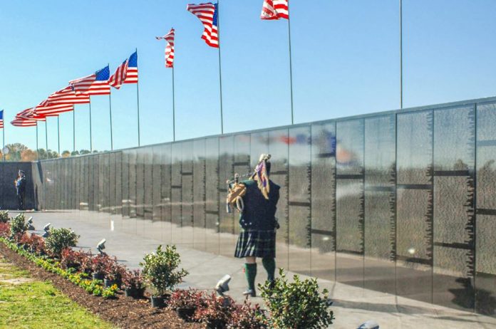 A Vietnam veteran plays the bagpipes at the Dignity Memorial Vietnam Wall. The exhibit crisscrosses the country each year, allowing millions of visitors to see and touch the black, mirror-like surface inscribed with the names of more than 58,000 Americans who died or are missing in Vietnam. The wall honors all U.S. veterans and is dedicated to Vietnam veterans. Photo/U.S. Navy .