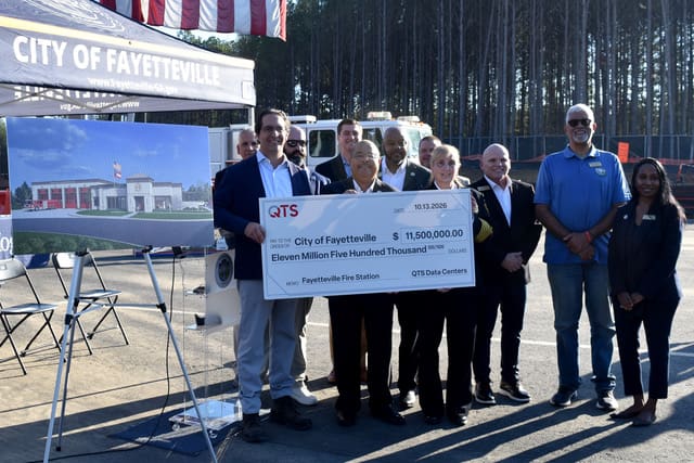 Officials hold an oversized $11.5 million check from QTS to the City of Fayetteville for Fire Station 93 beside a rendering of the new station