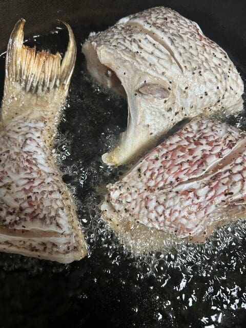 Pieces of hog snapper frying in hot oil in a cast-iron pan