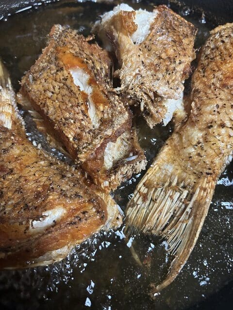 Golden fried hog snapper pieces and a crispy tail in a pan