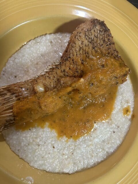 Fried hog snapper topped with sauce over a plate of grits