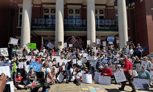 A crowd holding protest signs gathers on the steps of the Coweta County Courthouse in Newnan.