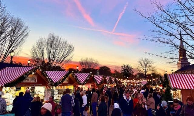 Shoppers fill a lane of red-and-white striped market stalls at sunset at the Atlanta Christkindl Market.