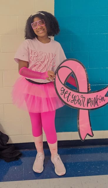 A Flat Rock Middle student in pink holds a pink ribbon sign that says Get Your Pink On.
