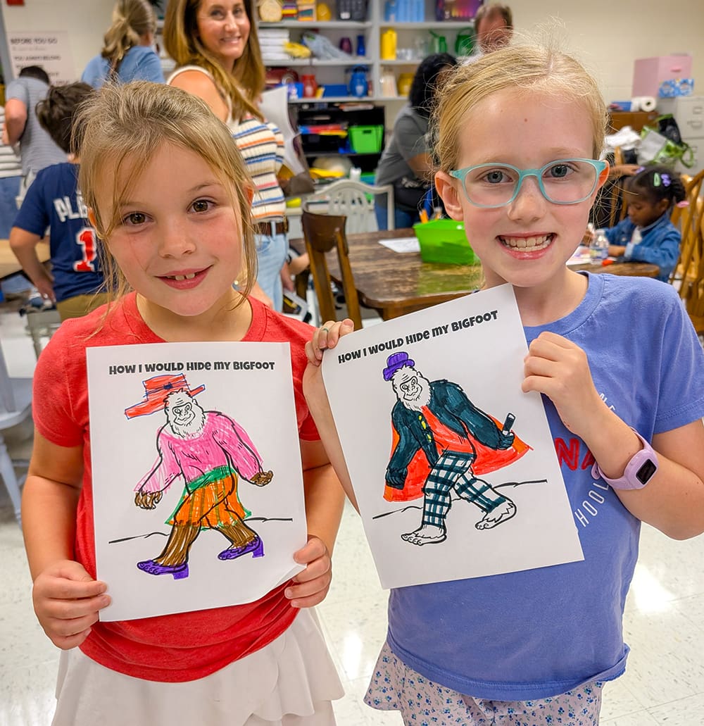 Two students hold up their Big Foot drawings