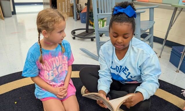 Two Braelinn Elementary students sit on the classroom floor reading a book together