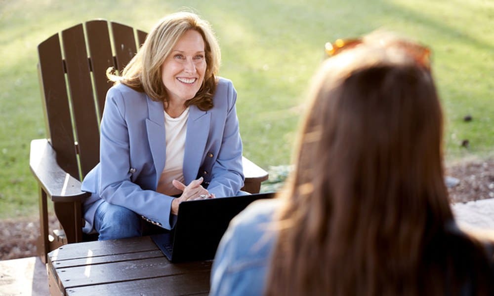 Maura Keller, Democratic candidate for Georgia's 3rd Congressional District, smiles during an interview seated outdoors at a wooden table with a laptop.